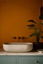 Modernes Badezimmer mit Wänden in Ashes of Marigold. Das warme, erdige Orange bildet einen spannenden Kontrast zum Waschtisch in Perpetual Blue und dunklen Details in Vulcan.